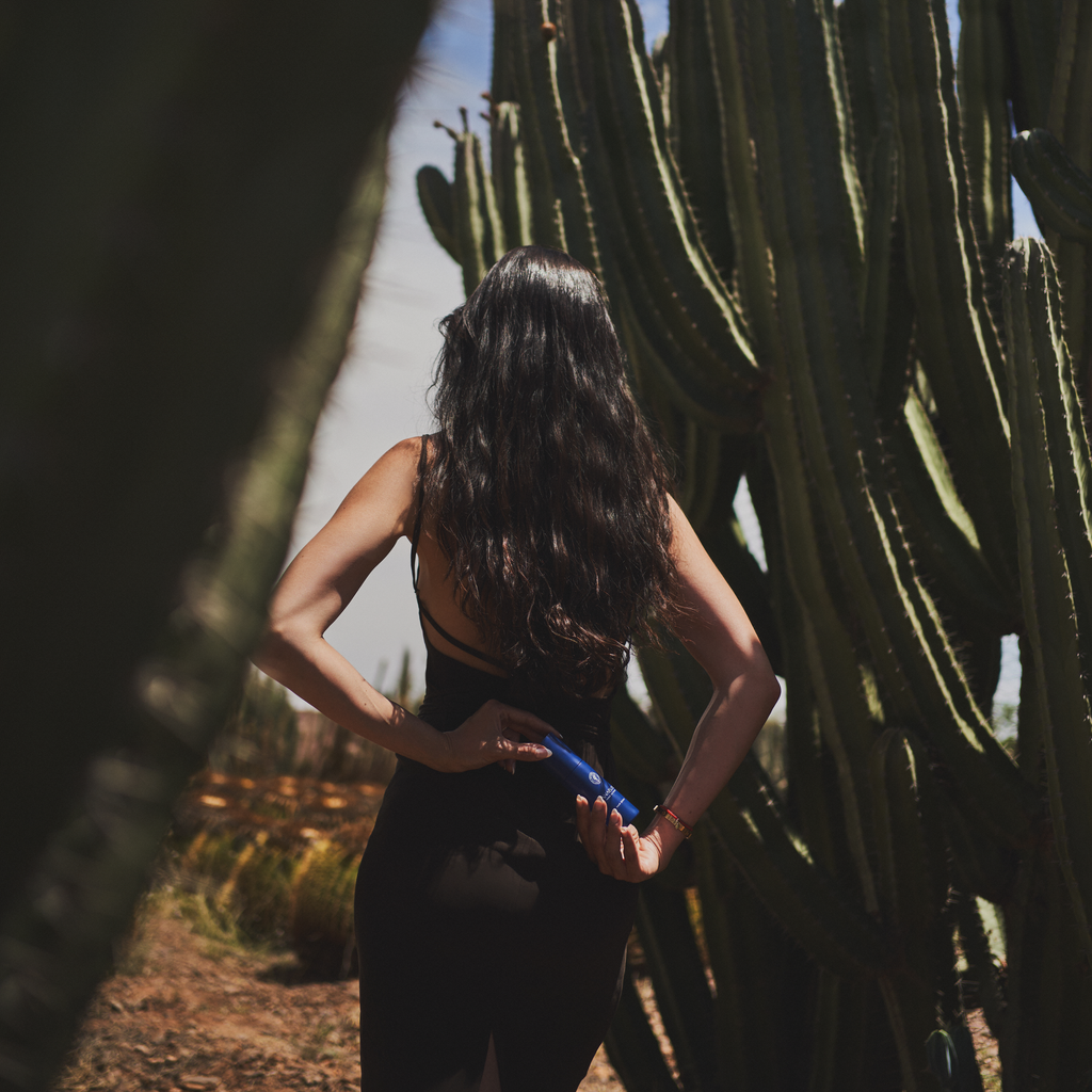 Lauren Perez, founder, holding hair serum behind her back surrounded by cacti
